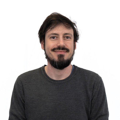 Portrait of a smiling man with dark hair and a beard, wearing a dark gray sweater, against a white background.