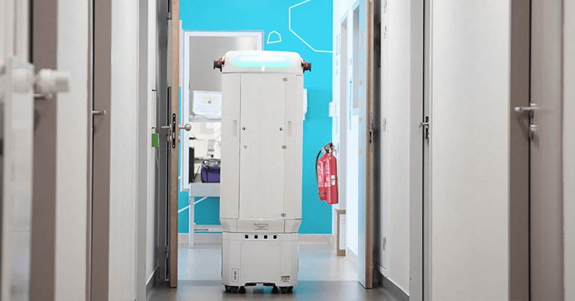 White autonomous service robot in a bright hallway with a blue accent wall ahead.