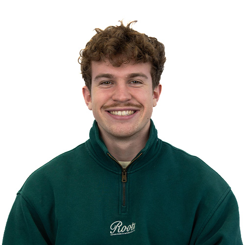 Smiling young man with curly brown hair wearing a green pullover, facing the camera with a cheerful expression.