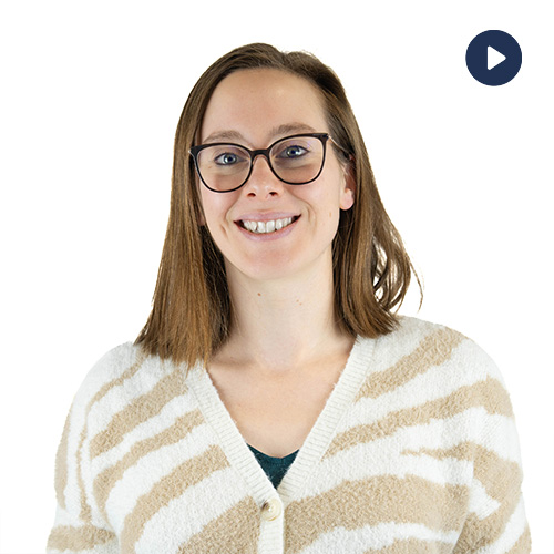 Smiling woman with glasses wearing a beige striped cardigan; play button overlay in the top-right indicates a video.
