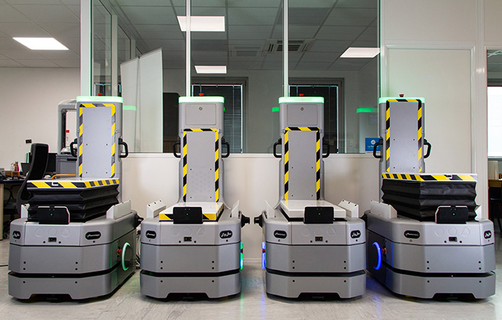 Four autonomous delivery robots with yellow/black safety tape, lined up in a clean lab showroom room.