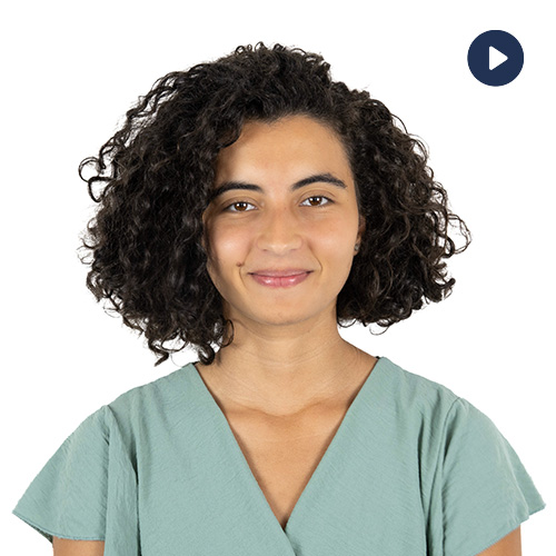 Portrait of a woman with curly hair in green scrubs, smiling at the camera (video thumbnail). Related to a healthcare professional.