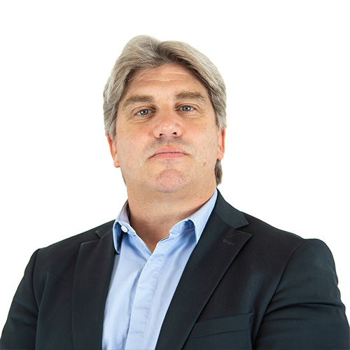 Confident middle-aged man in a dark suit jacket and light blue shirt, standing against a white background.