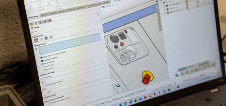 Screenshot of CAD software on a laptop showing a device enclosure with a red button and yellow control knob.